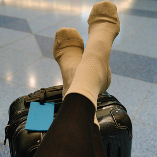 Woman enjoying ankle brace like support in her crew compression socks while resting her feet on a suitcase